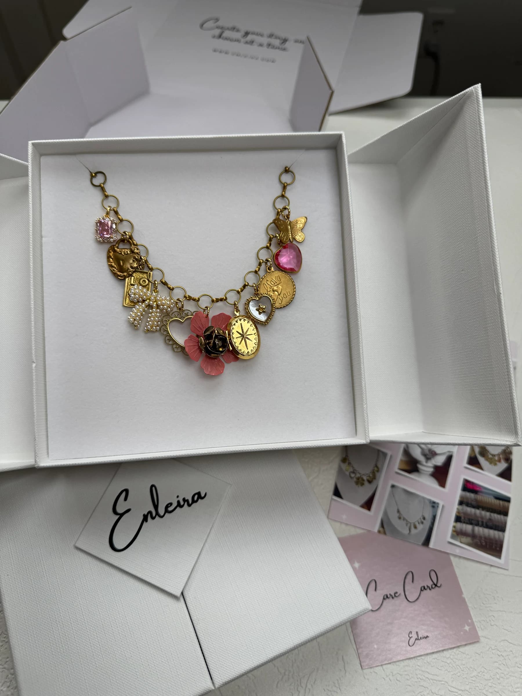 A custom 18k gold plated charm necklace with pink and pearl accents, displayed in an elegant white gift box, by Enleira.